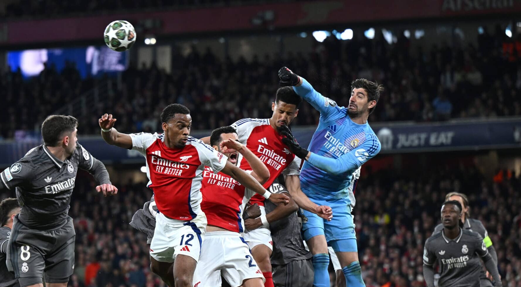 Real Madrid goalkeeper Thibaut Courtois of Real Madrid punches the ball clear as Jurrien Timber, Mikel Merino and William Saliba of Arsenal challenge during the UEFA Champions League 2024/25 Quarter Final First Leg match between Arsenal FC and Real Madrid C.F. at Emirates Stadium on April 08, 2025 in London, England.