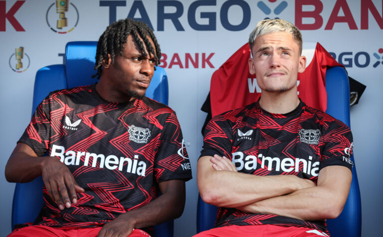 Florian Wirtz (R) and Jeremie Frimpong (L) of Bayer 04 Leverkusen sit on the bench prior to the DFB-Pokal match between FC Carl Zeiss Jena and Bayer 04 Leverkusen at Ernst-Abbe-Sportfeld on August 28, 2024 in Jena, Germany.