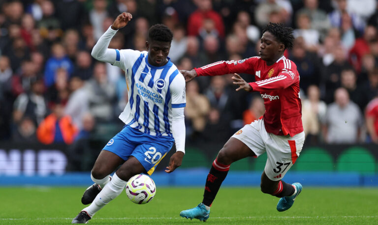 Manchester United - Carlos Baleba of Brighton & Hove Albion runs with the ball under pressure from Kobbie Mainoo of Manchester United during the Premier League match between Brighton & Hove Albion FC and Manchester United FC at Amex Stadium on August 24, 2024 in Brighton, England.