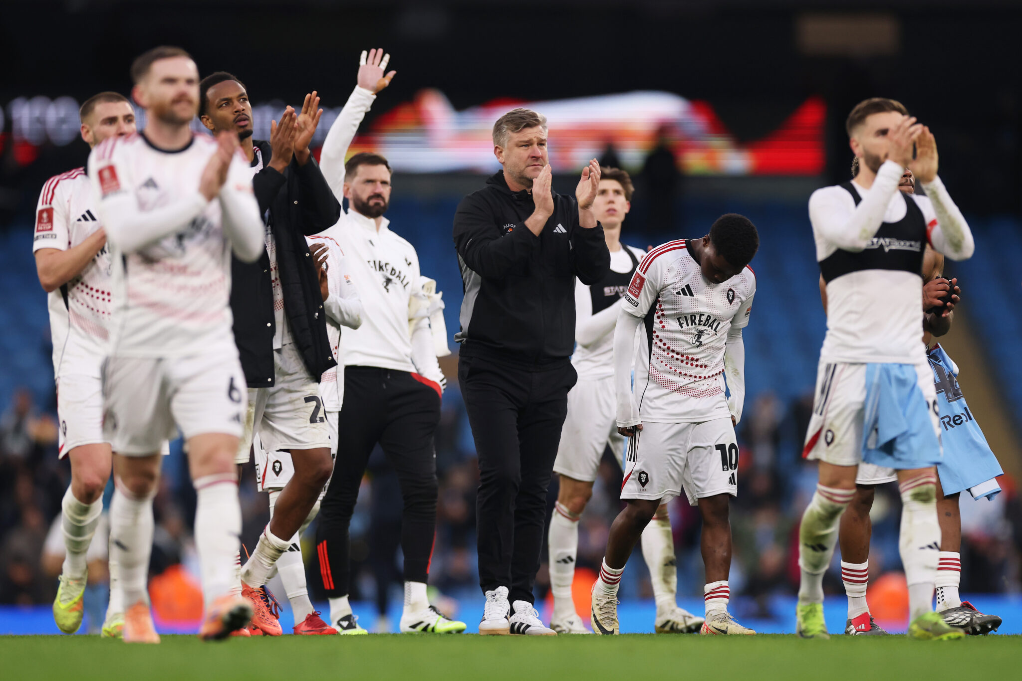 Karl Robinson, Manager of Salford City, acknowledges the fans with his players after the Emirates FA Cup Fourth Round match between Manchester City and Salford City at Etihad Stadium on February 14, 2026 in Manchester, England.